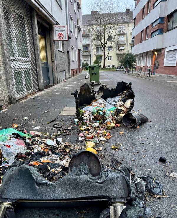 Zwei verbrannte Container liegen auf der Straße, zwischen ihnen der ganze Müll.