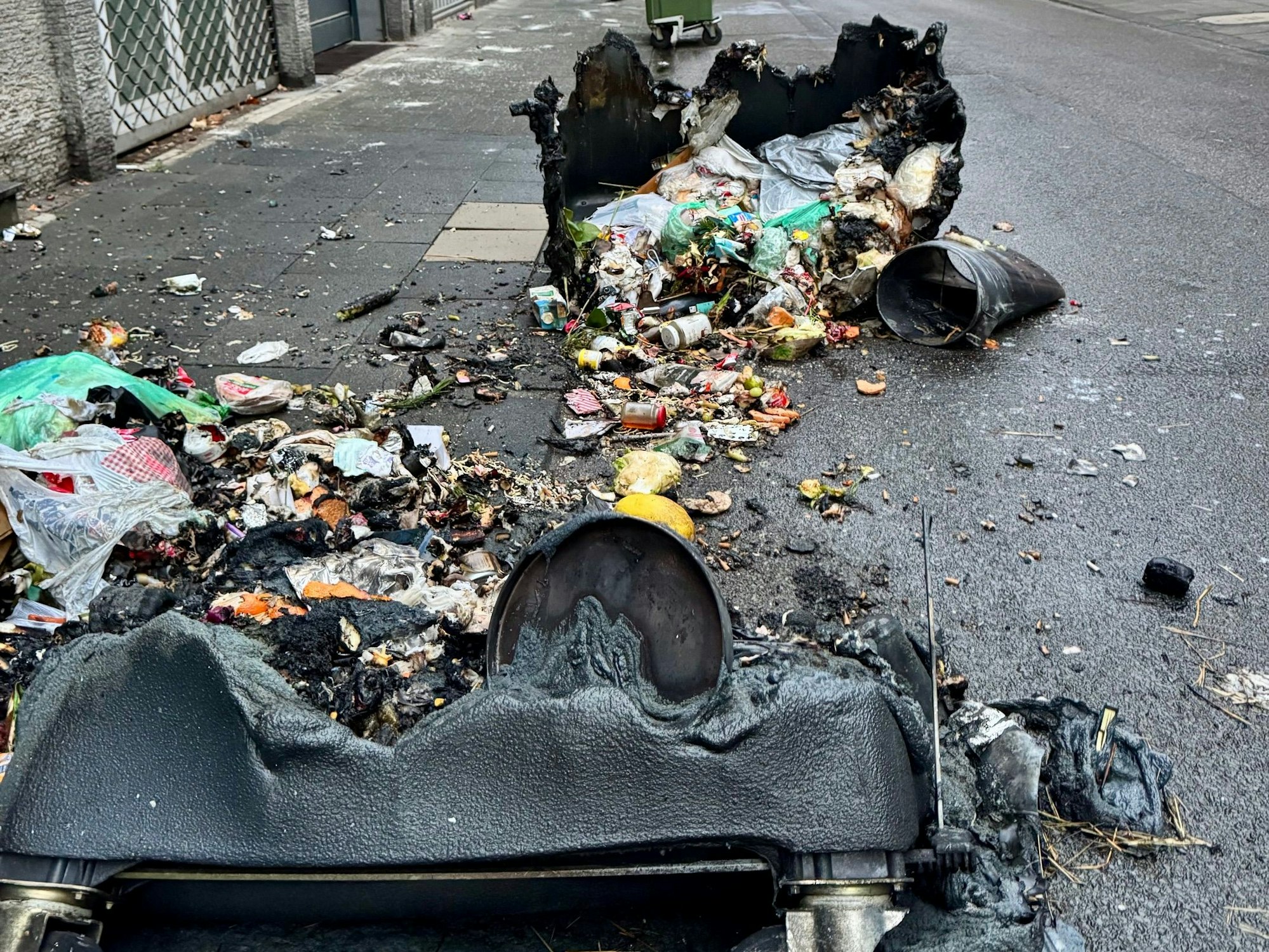 Zwei verbrannte Container liegen auf der Straße, zwischen ihnen der ganze Müll.