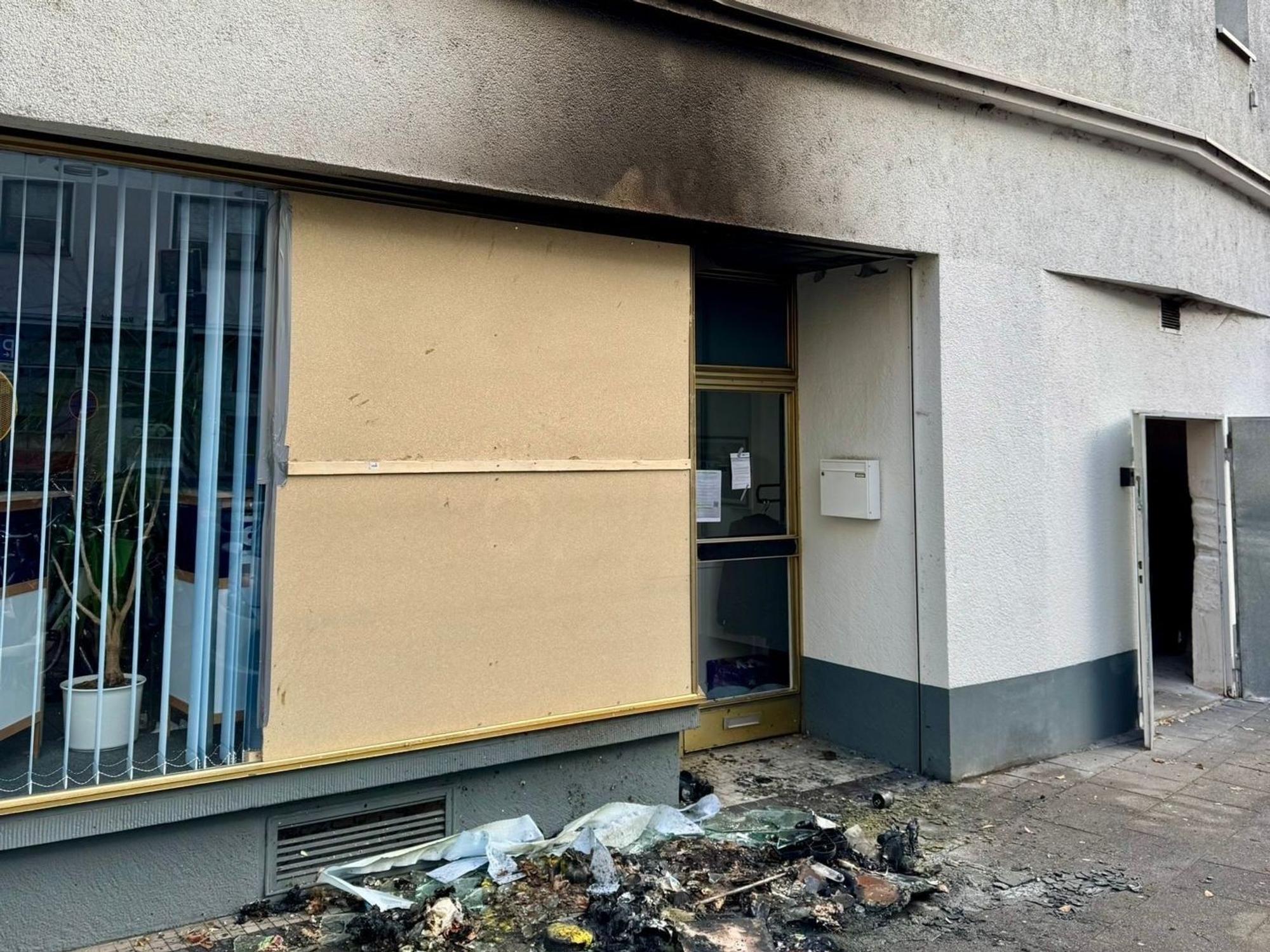 Die Reste eines verbrannten Containers liegen vor einem Haus, an dessen Fassade eine Rußspur ist.