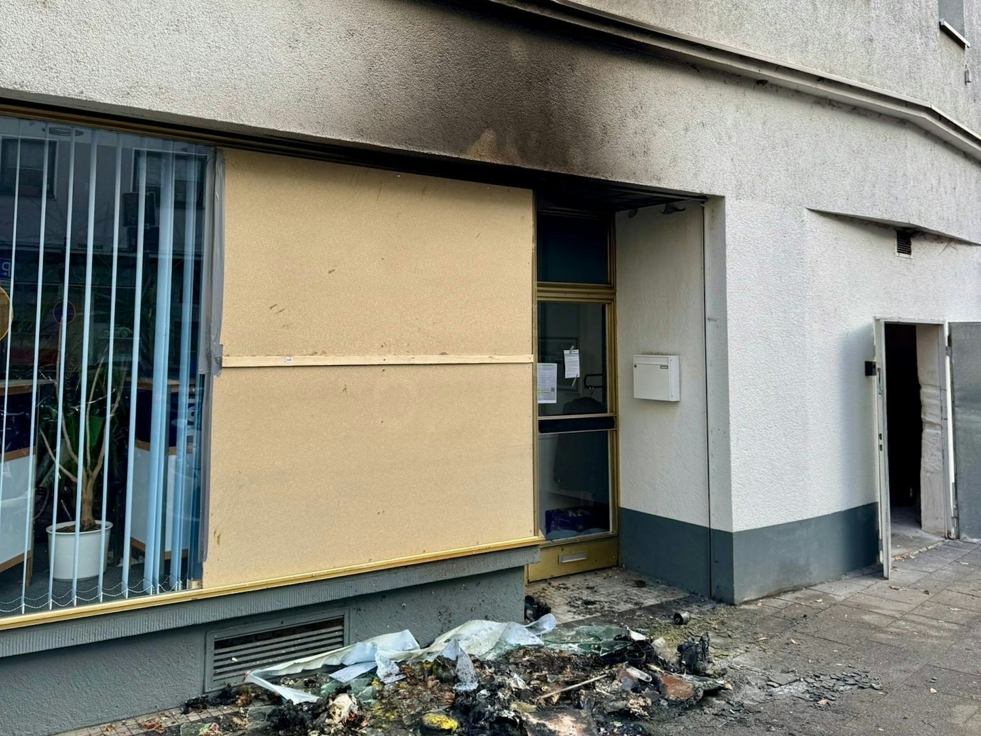 Die Reste eines verbrannten Containers liegen vor einem Haus, an dessen Fassade eine Rußspur ist.