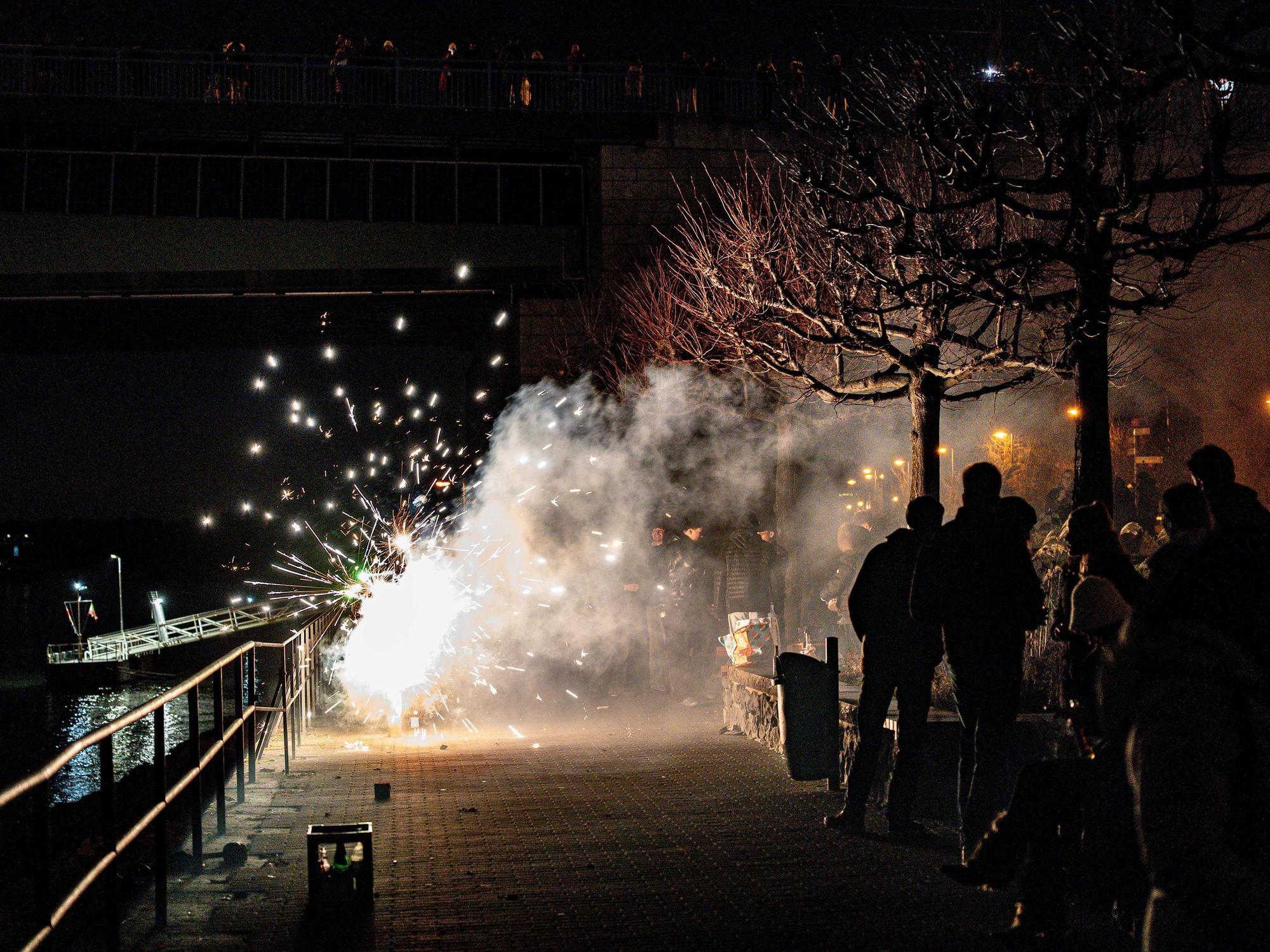 Feiernde zünden Feuerwerk in der Silvesternacht am Rheinufer an der Kennedybrücke.