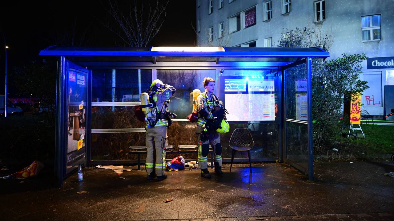 Erschöpfte Feuerwehrmänner stehen nach einem Einsatz während der Silvesternacht nach einer Brandbekämpfung in Berlin an einer Bushaltestelle.