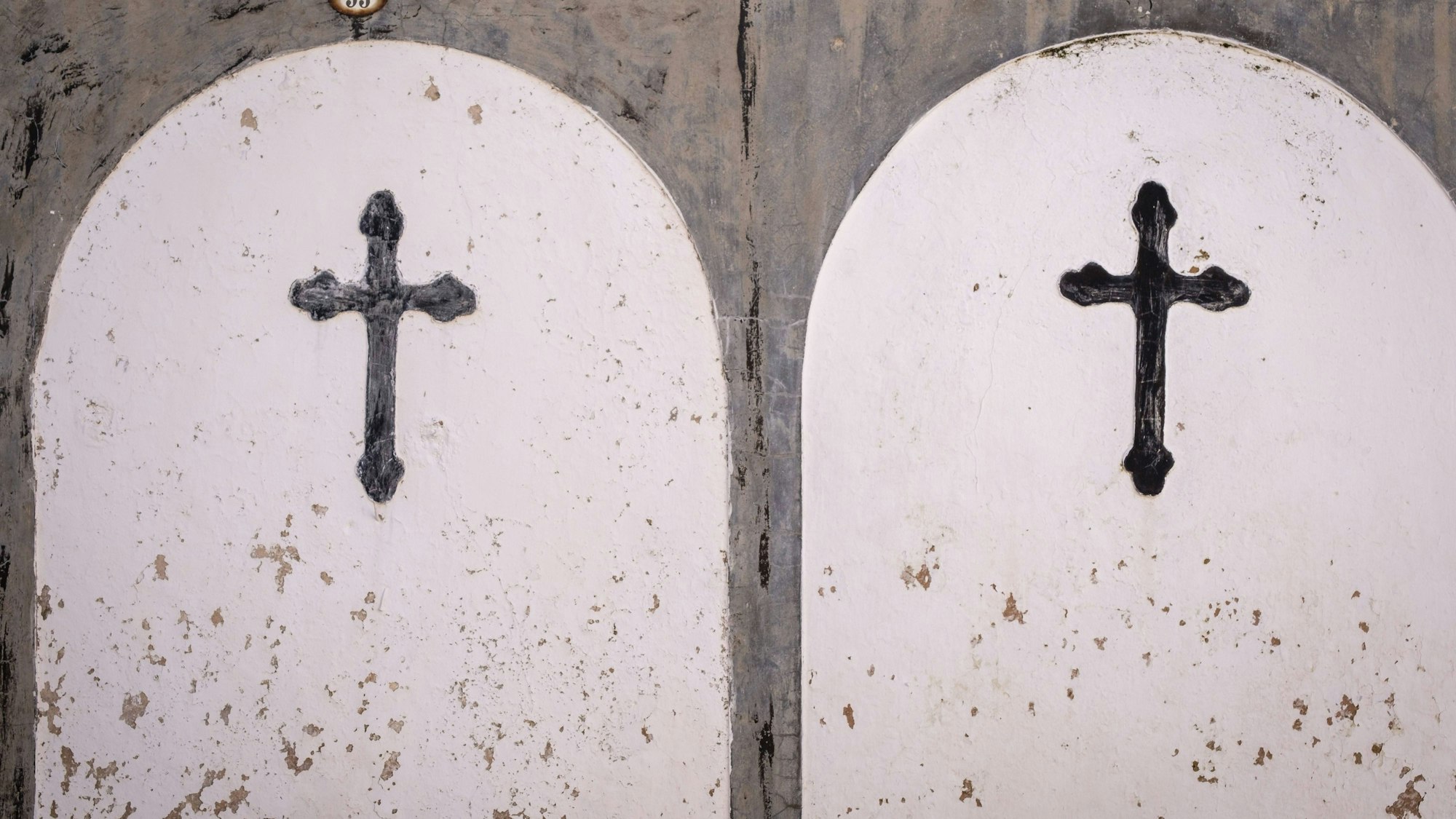 Zwei Kreuze auf verwitterter Wandstruktur