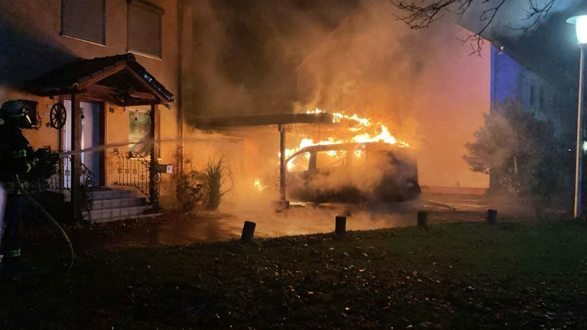 Feuerwehr löscht brennenden Camper-Van in einem Carport.