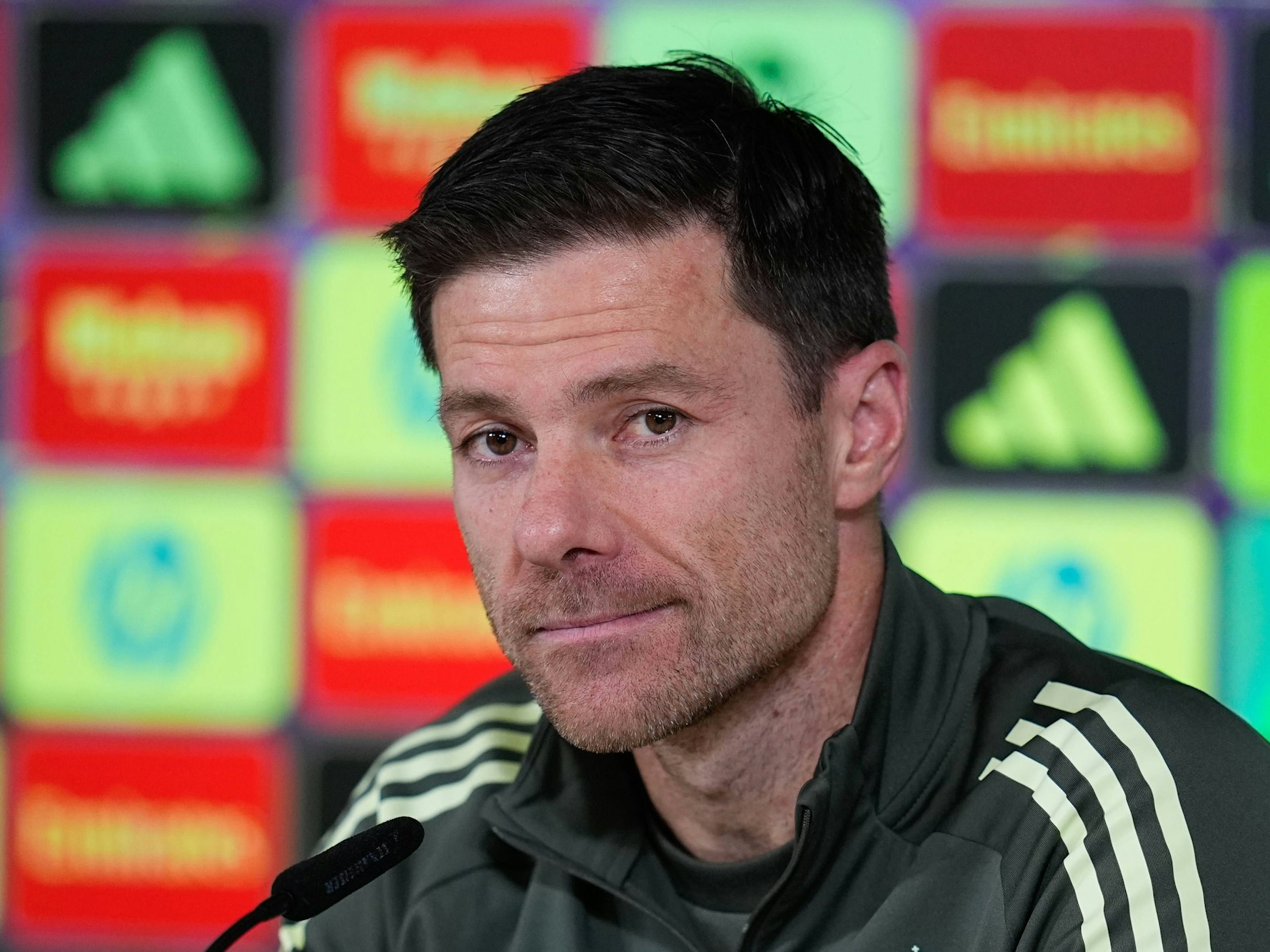 Trainer Xabi Alonso schaut bei einer Presskonferenz in die Runde. Vor ihm steht ein Mikrofon.