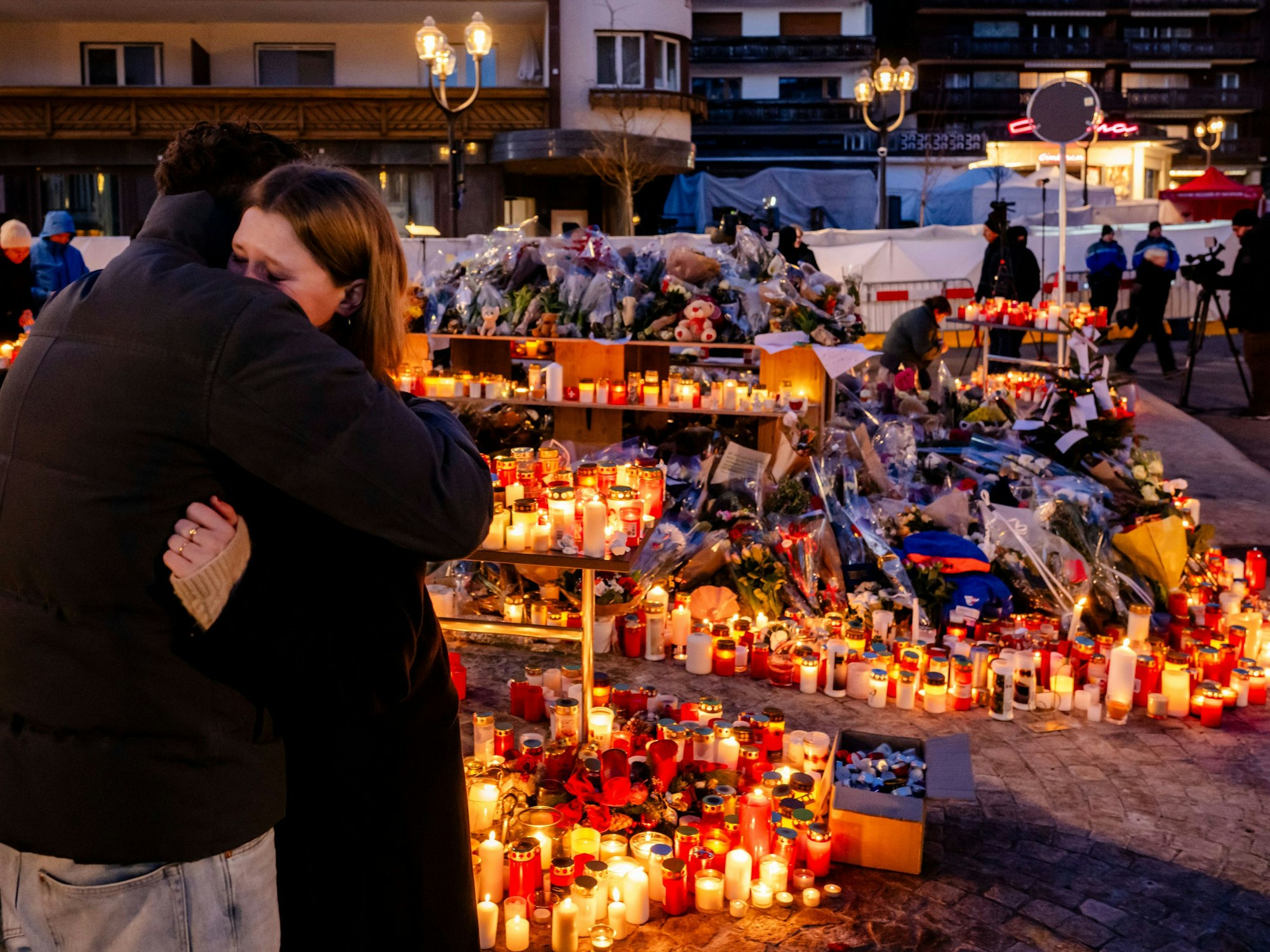 Ein Meer von brennenden Kerzen steht am Unglücksort, auch viele Blumen wurden niedergelegt. Davor umarmt sich ein Paar.