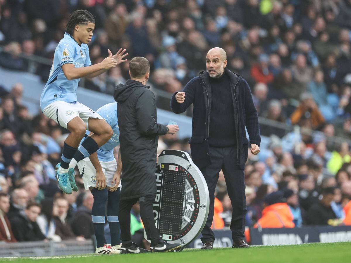 Jahmai Simpson-Pusey springt im Trikot von Manchester City in die Luft, Trainer Pep Guardiola gestikuliert dabei.