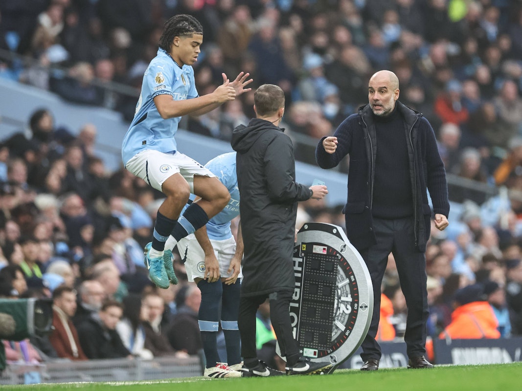 Jahmai Simpson-Pusey springt im Trikot von Manchester City in die Luft, Trainer Pep Guardiola gestikuliert dabei.