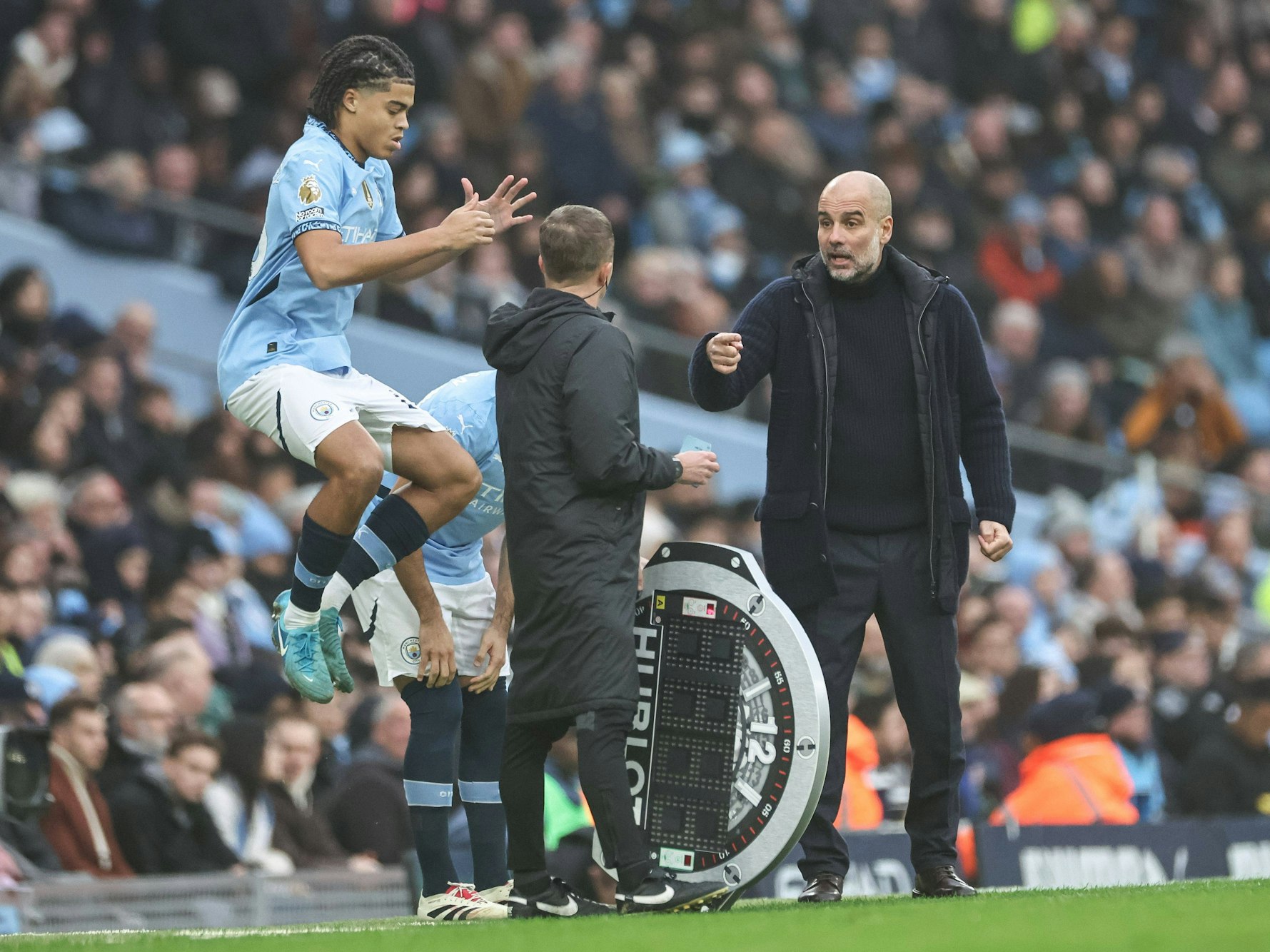 Jahmai Simpson-Pusey springt im Trikot von Manchester City in die Luft, Trainer Pep Guardiola gestikuliert dabei.