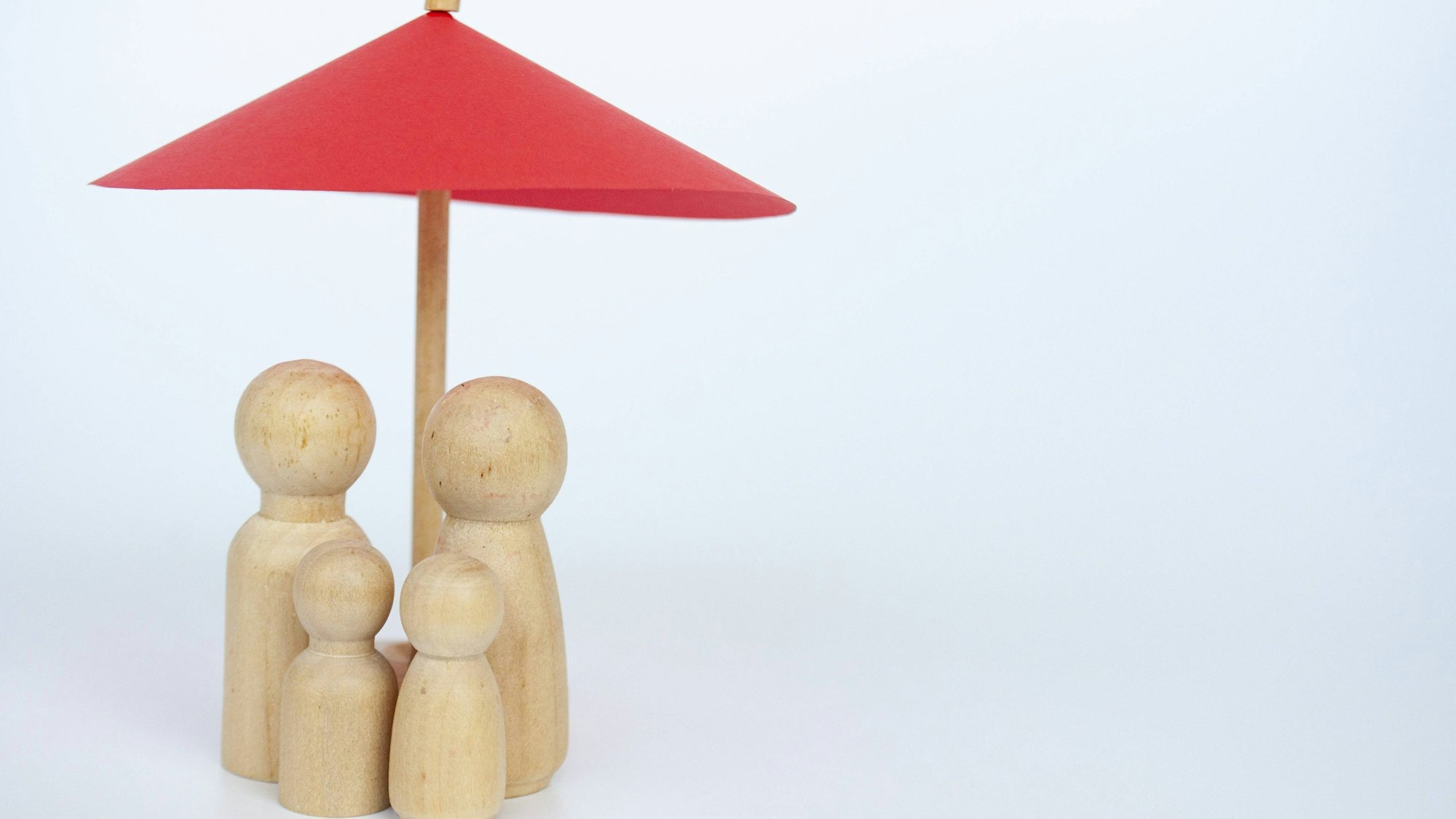 Roter Regenschirm über Holzfiguren einer Familie