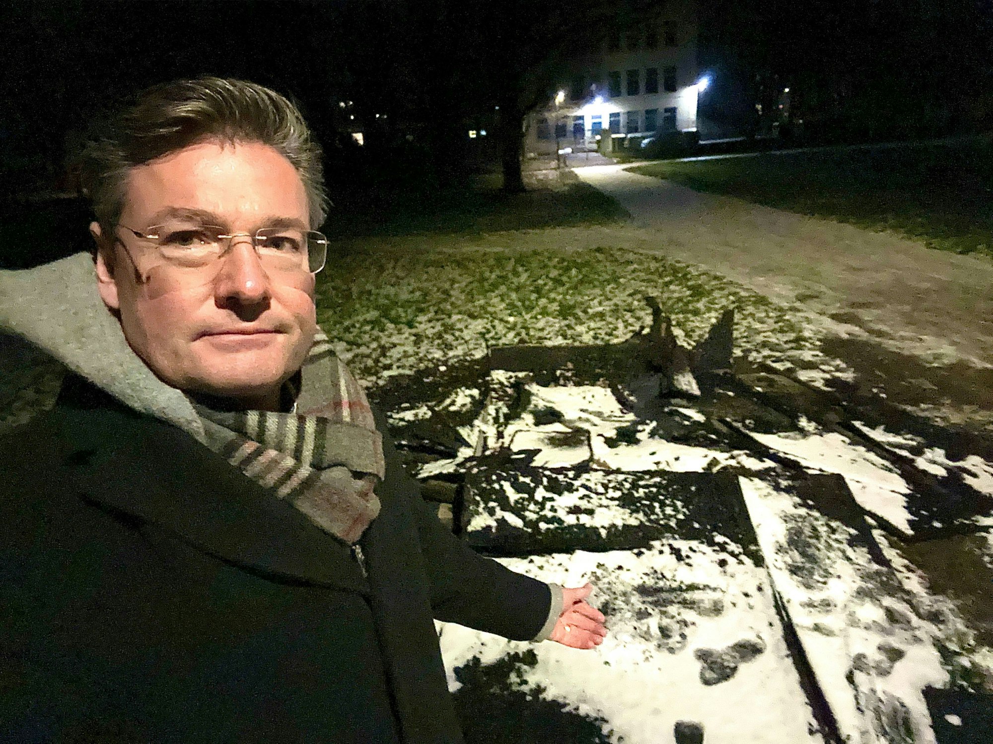 Ein Mann steht vor einem Haufen verkohlter Bretter, die auf einer Rasenfläche liegen.