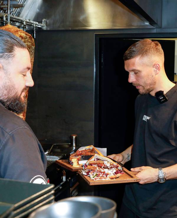 Lukas Podolski hält in seiner Mangal-Filiale zwei Döner in der Hand.
