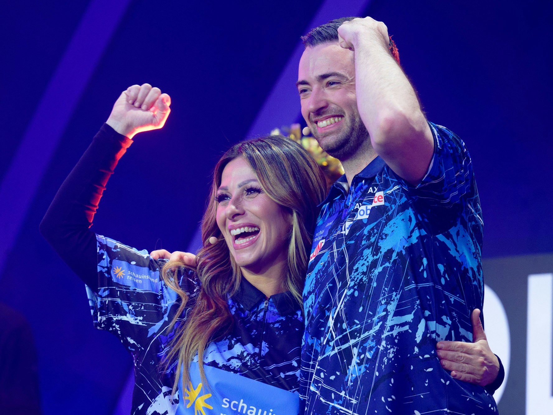 Gülcan Kamps und Dart-Profi Luke Humphries stehen bei der Promi-Darts-WM 2026 auf der Bühne.