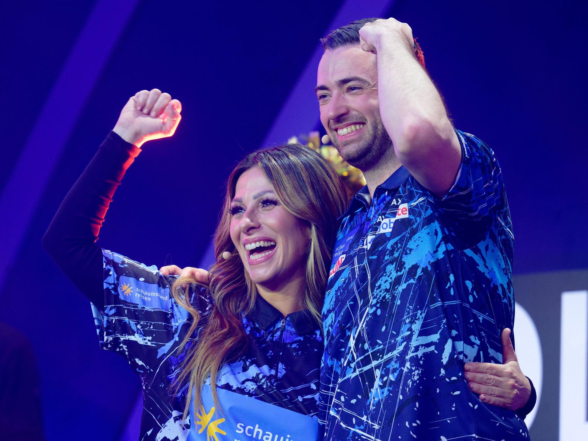 Gülcan Kamps und Dart-Profi Luke Humphries stehen bei der Promi-Darts-WM 2026 auf der Bühne.