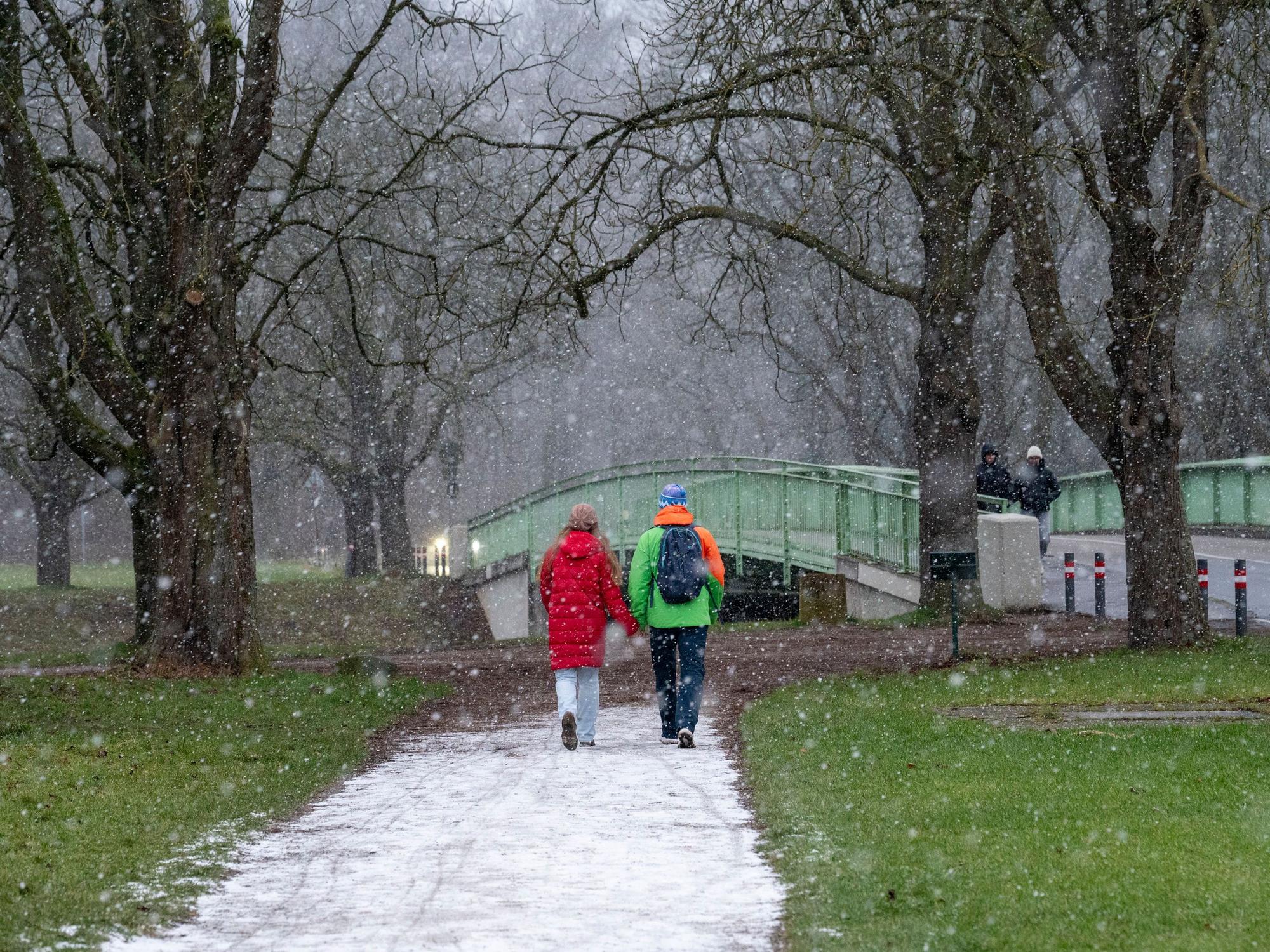 Ein Paar geht Hand in Hand über einen schneebedeckten Weg, auf der Wiese rechts und links liegt kein Schnee.