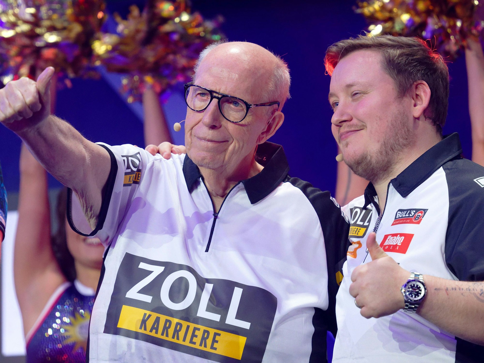 Reiner Calmund und Dart-Profi Martin Schindler stehen bei der Promi-Darts-WM 2026 auf der Bühne.