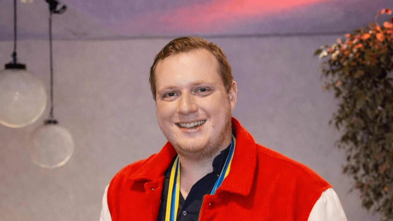 Nik Lewin steht mit Orden um den Hals vor einem Saal.