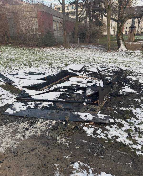 Verkohlte Bretter liegen auf einer verschneiten Rasenfläche.