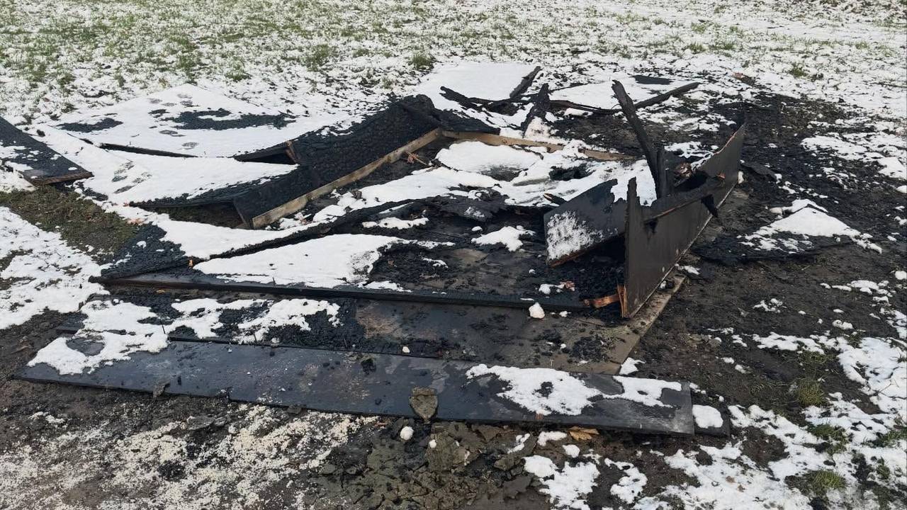 Verkohlte Bretter liegen auf einer verschneiten Rasenfläche.