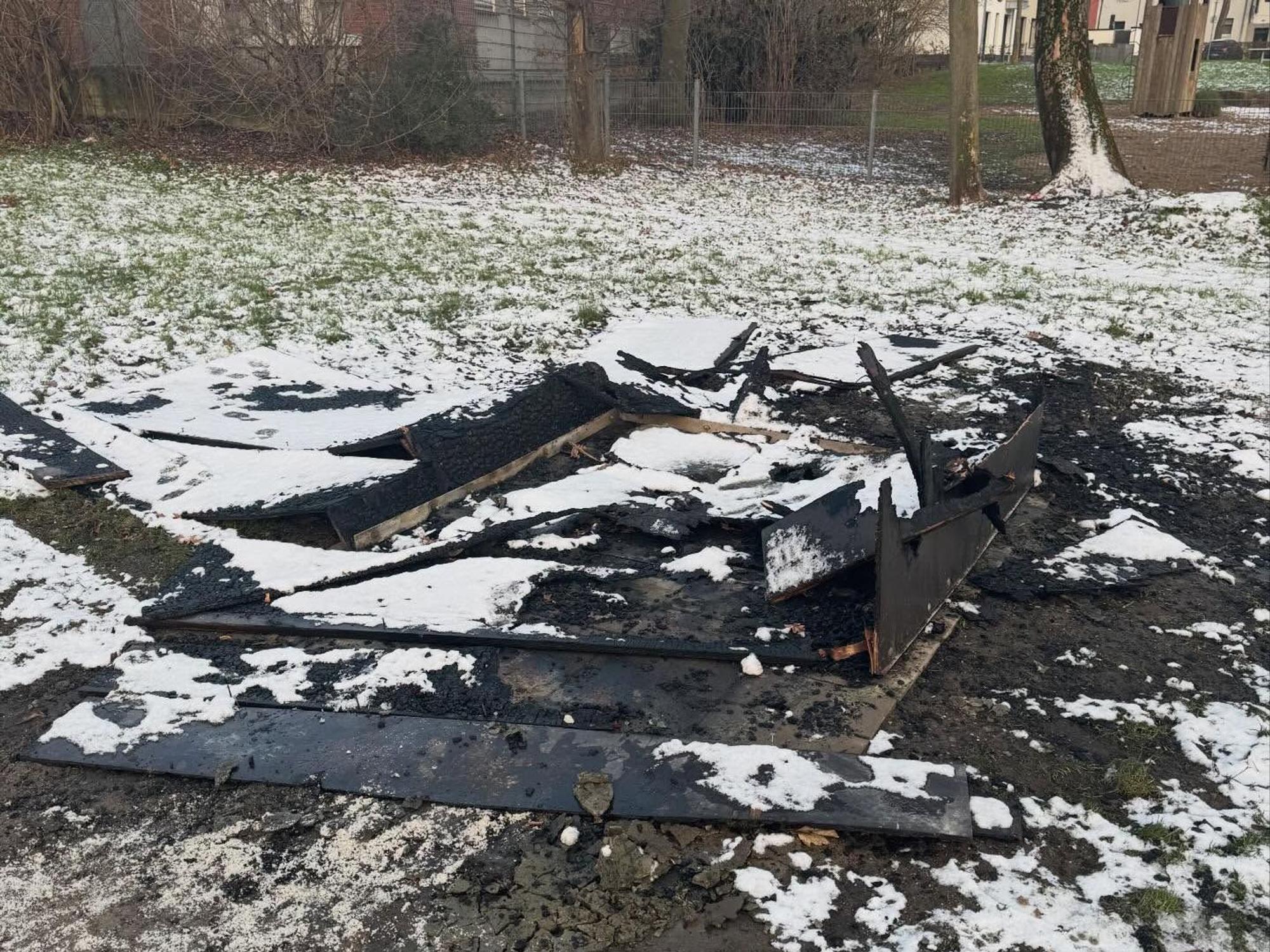 Verkohlte Bretter liegen auf einer verschneiten Rasenfläche.