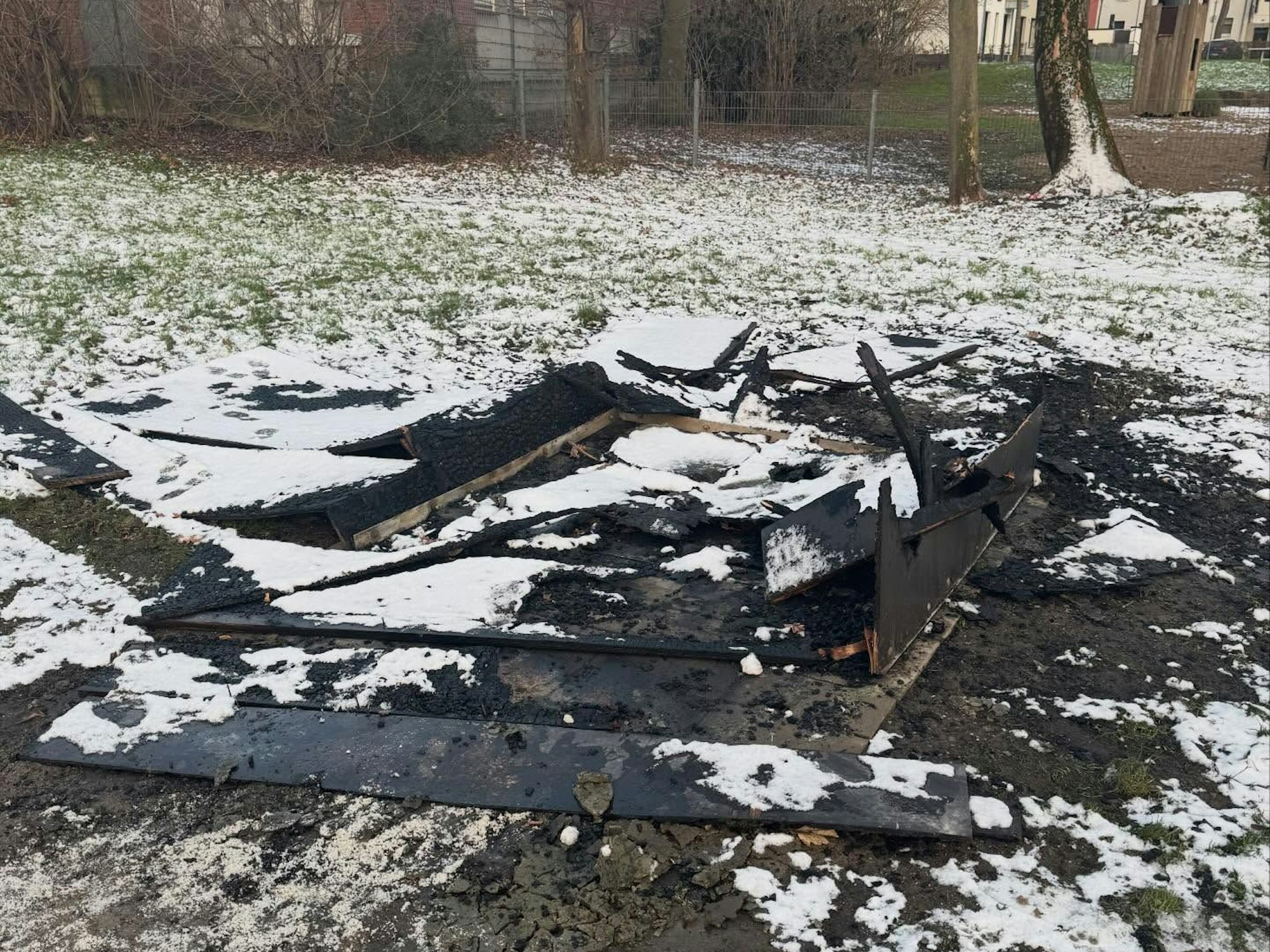 Verkohlte Bretter liegen auf einer verschneiten Rasenfläche.