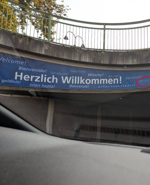 Auf einem Schild steht das Willkommen in verschiedenen Sprachen, ein japanischer Schriftzug ist eingekringelt worden.