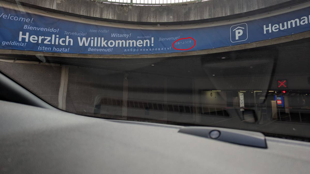 Auf einem Schild steht das Willkommen in verschiedenen Sprachen, ein japanischer Schriftzug ist eingekringelt worden.