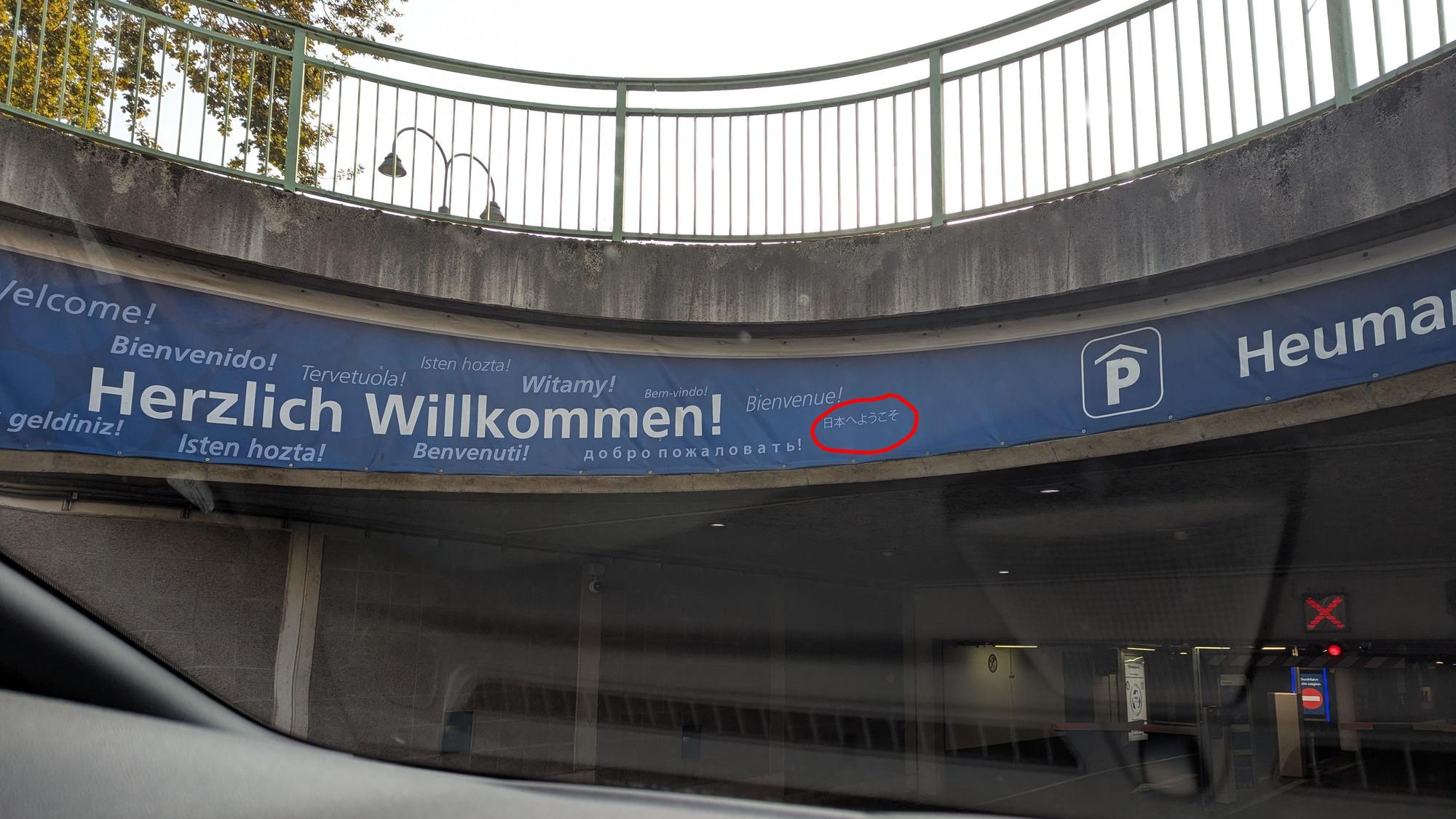 Auf einem Schild steht das Willkommen in verschiedenen Sprachen, ein japanischer Schriftzug ist eingekringelt worden.