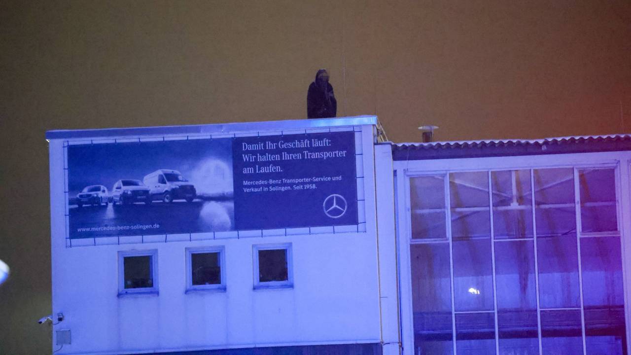Eine Person harrt im Dunkeln auf einem Gebäudedach aus.