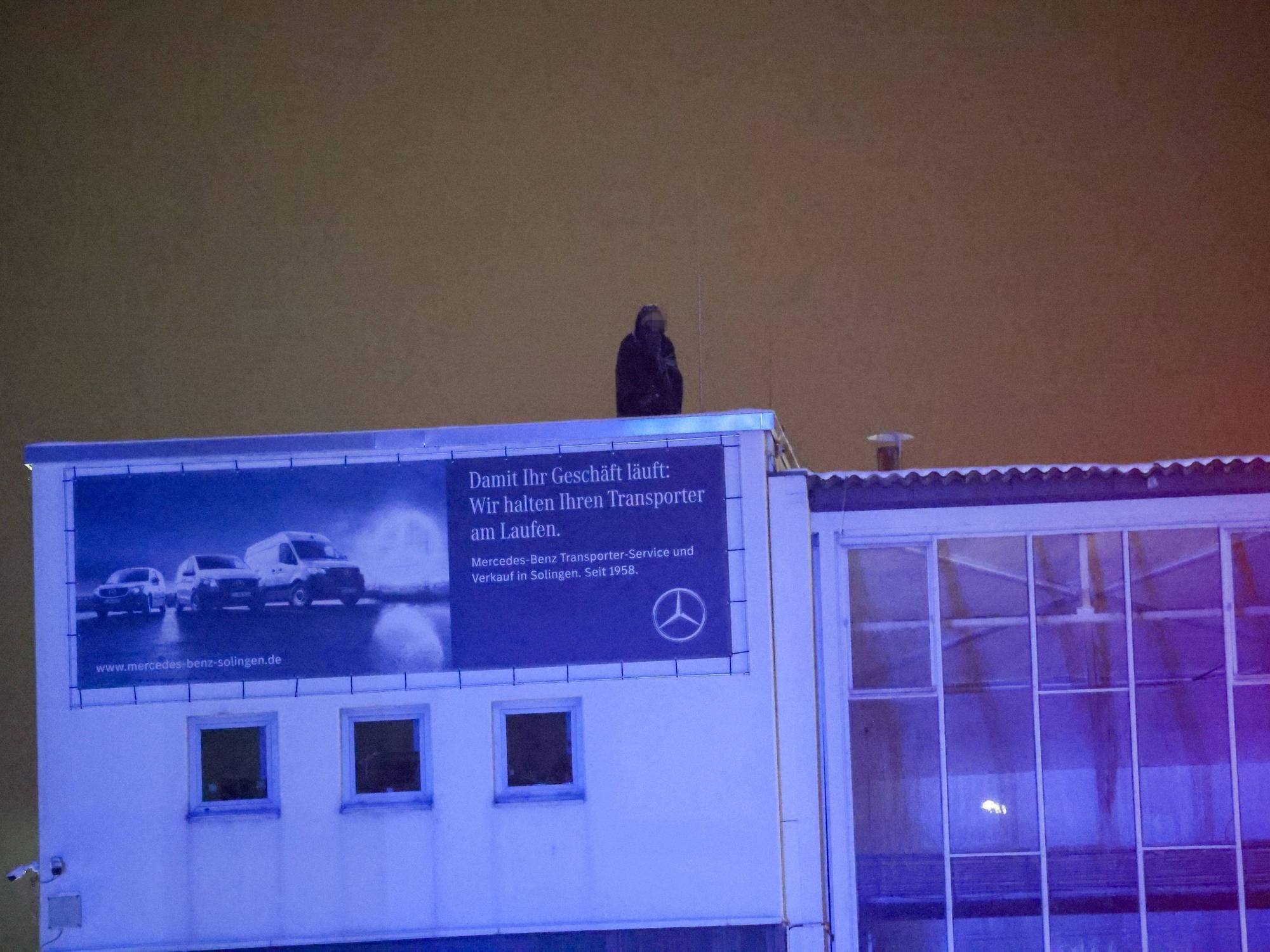 Eine Person harrt im Dunkeln auf einem Gebäudedach aus.