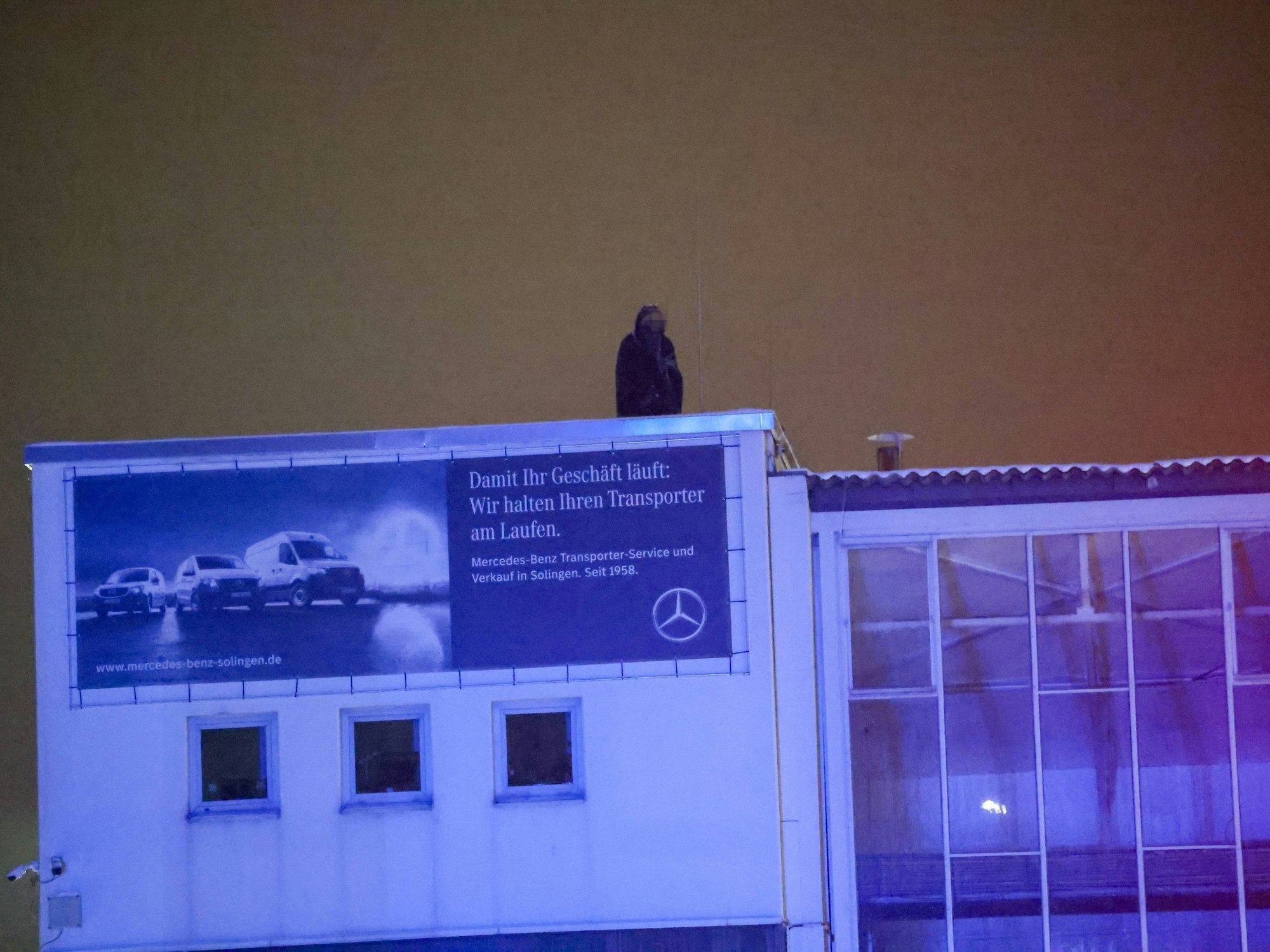 Eine Person harrt im Dunkeln auf einem Gebäudedach aus.