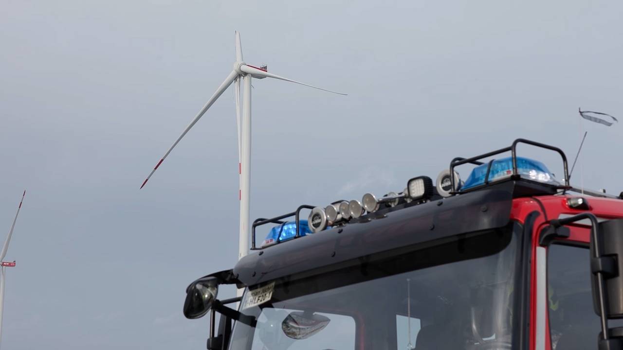 Ein Fahrzeug der Feuerwehr steht vor einem Windrad.