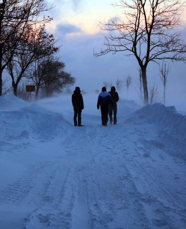 Spaziergänger stehen auf der Ostseeinsel Fehmarn auf einer Straße von Burg in Richtung Meeschendorf bei Sonnenaufgang vor einer Schneewehe (Archivbild).