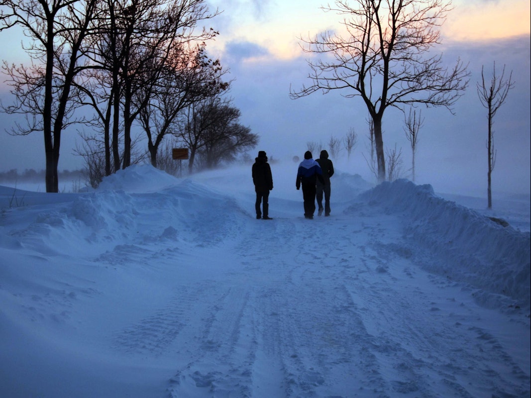 Spaziergänger stehen auf der Ostseeinsel Fehmarn auf einer Straße von Burg in Richtung Meeschendorf bei Sonnenaufgang vor einer Schneewehe (Archivbild).