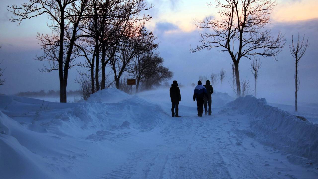 Spaziergänger stehen auf der Ostseeinsel Fehmarn auf einer Straße von Burg in Richtung Meeschendorf bei Sonnenaufgang vor einer Schneewehe (Archivbild).
