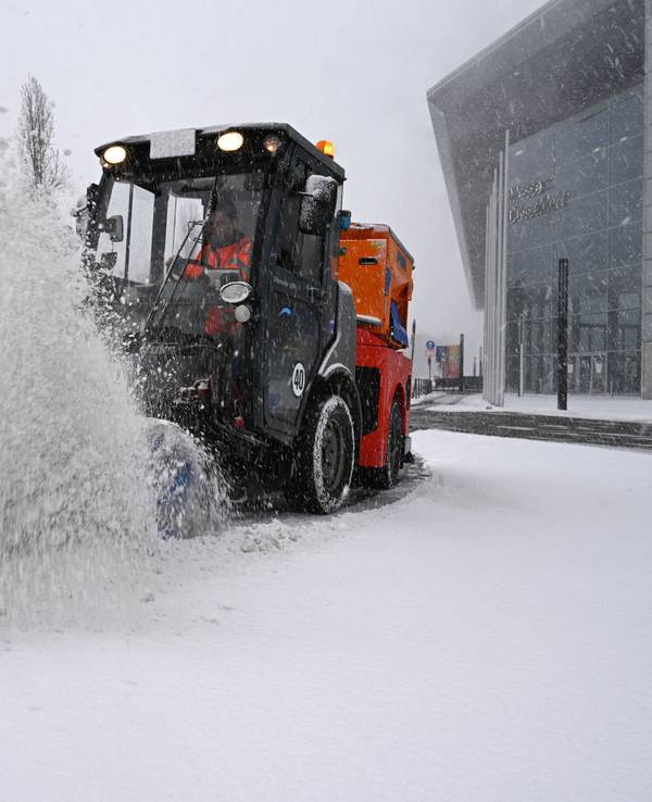 Ein Räumfahrzeug beseitigt bei dichtem Schneetreiben mit einer Bürste Schnee von einer Straße bei der Düsseldorfer Messe