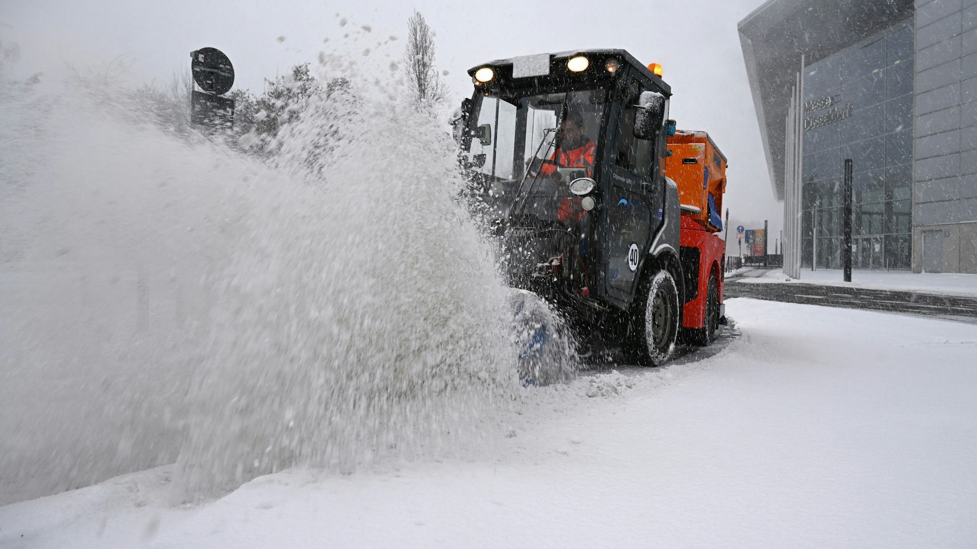 Ein Räumfahrzeug beseitigt bei dichtem Schneetreiben mit einer Bürste Schnee von einer Straße bei der Düsseldorfer Messe
