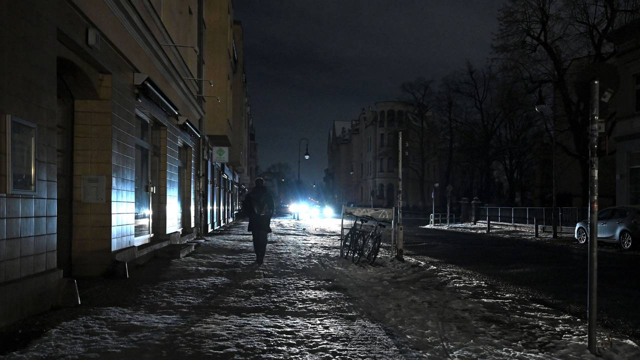 Eine Person läuft eine dunkle Straße in Berlin-Zehlendorf entlang, die nur durch einen Autoscheinwerfer erhellt wird.