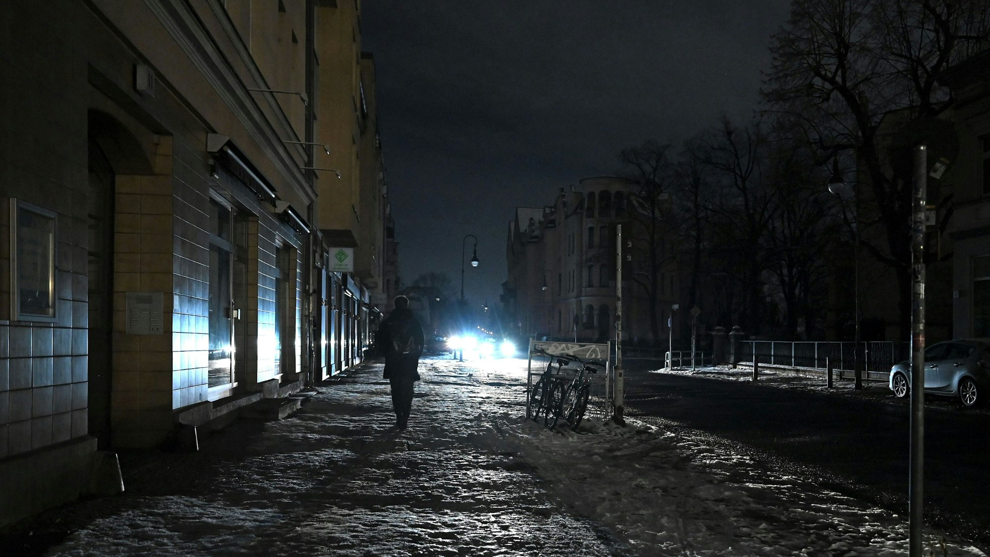 Eine Person läuft eine dunkle Straße in Berlin-Zehlendorf entlang, die nur durch einen Autoscheinwerfer erhellt wird.