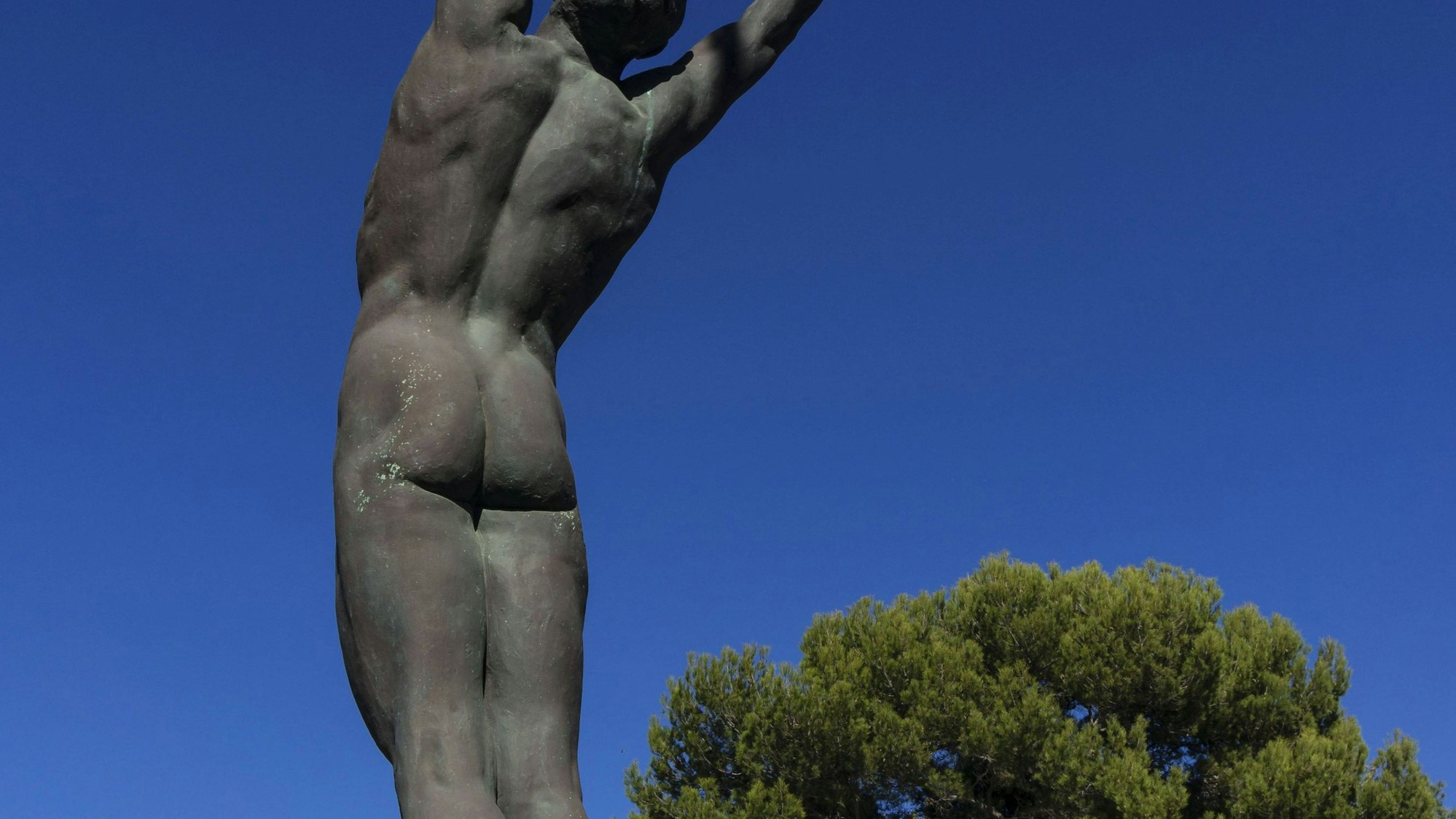 Icaro Skulptur unter blauem Himmel mit Bäumen