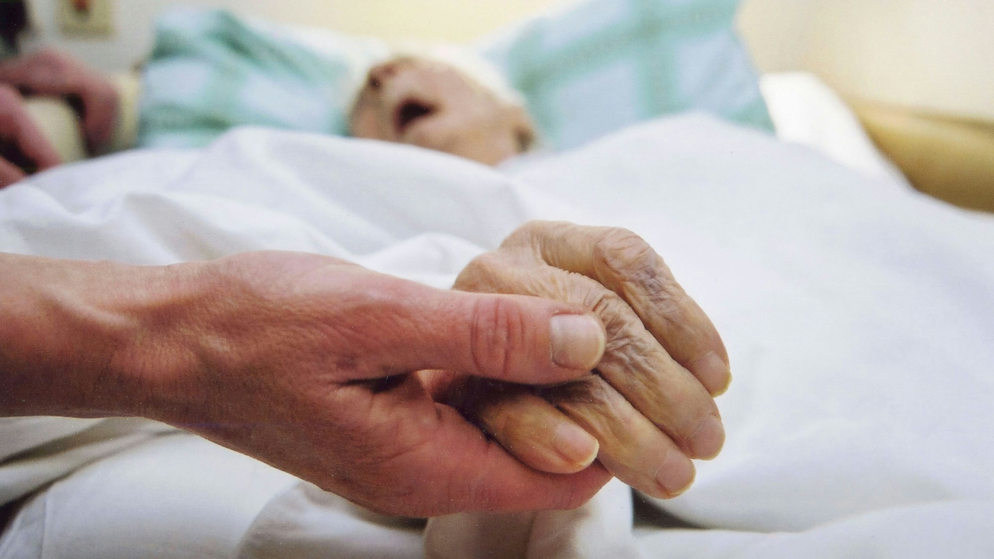 Eine Hand hält die eines älteren Menschen im Bett