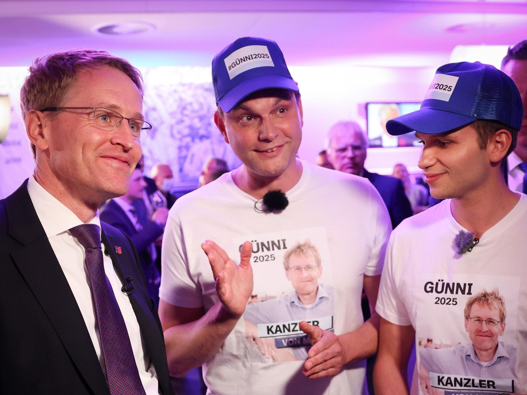 Die Moderatoren Lutz van der Horst (M) und Fabian Köster (r) von der ZDF-Satire-Sendung heute-Show stehen bei der Landtagswahl in Schleswig-Holstein neben Daniel Günther (CDU), Ministerpräsident von Schleswig-Holstein. Sie präsentieren T-Shirts und Mützen mit den Slogans "Günni 2025" und "Kanzler von Moin".