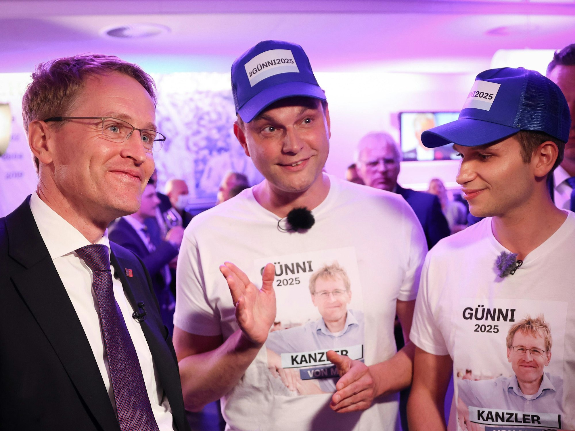 Die Moderatoren Lutz van der Horst (M) und Fabian Köster (r) von der ZDF-Satire-Sendung heute-Show stehen bei der Landtagswahl in Schleswig-Holstein neben Daniel Günther (CDU), Ministerpräsident von Schleswig-Holstein. Sie präsentieren T-Shirts und Mützen mit den Slogans "Günni 2025" und "Kanzler von Moin".