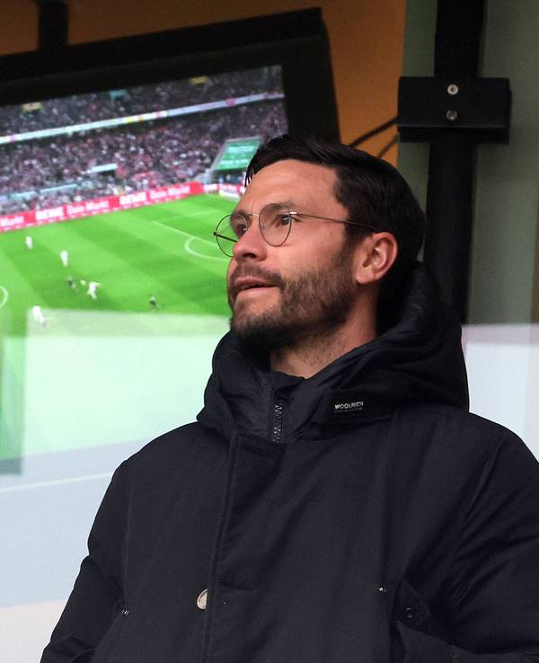 Jonas Hector steht vor einem Fernseher, auf dem ein Fußballspiel läuft.