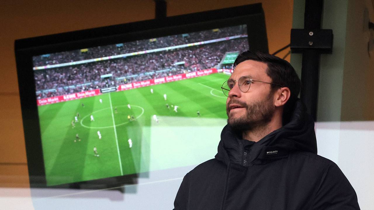 Jonas Hector steht vor einem Fernseher, auf dem ein Fußballspiel läuft.