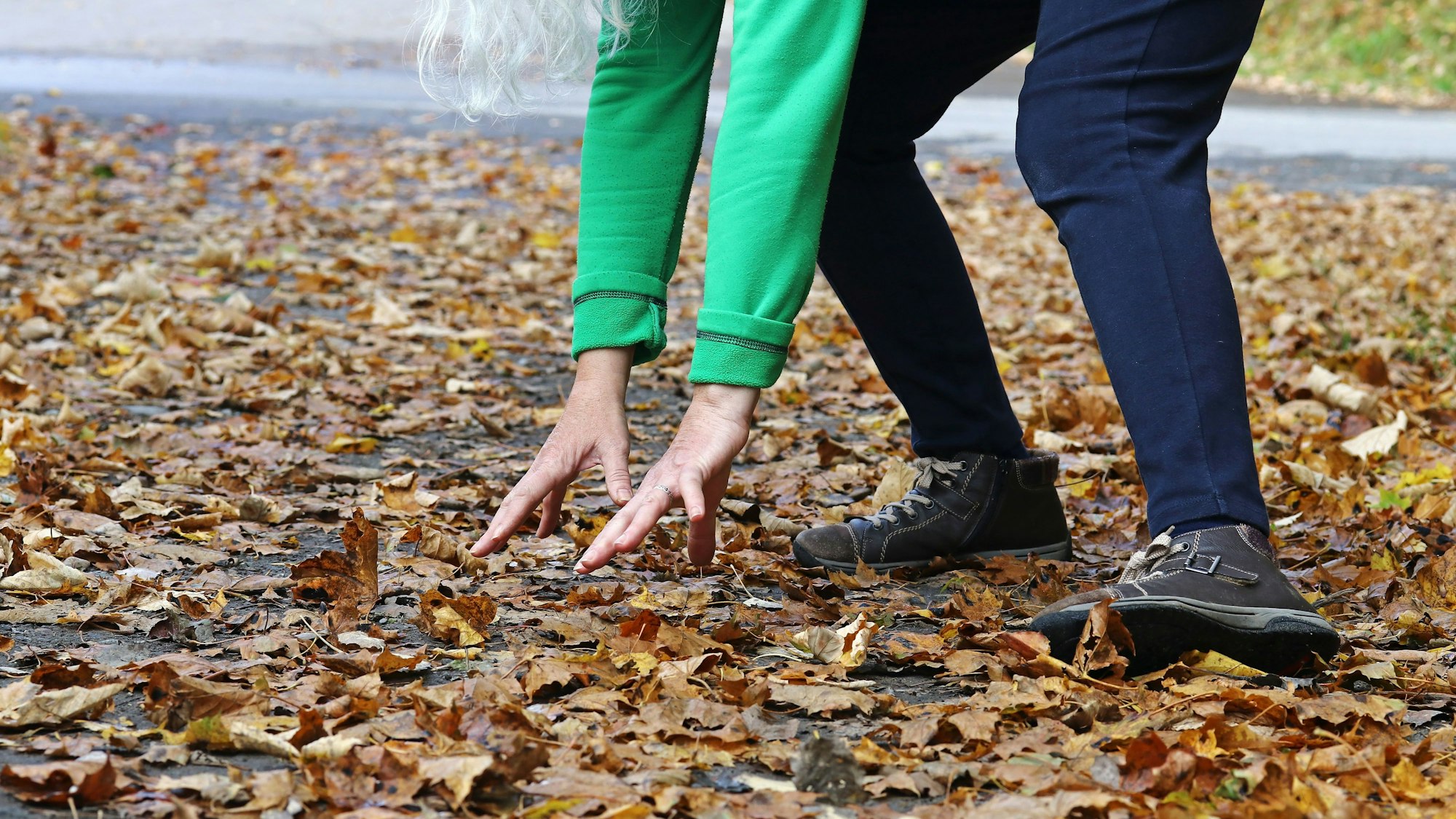 Frau bückt sich über herabgefallene Blätter