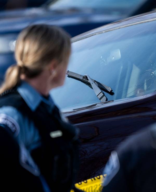 Polizeibeamte stehen vor einem Auto mit Einschussloch in der Windschutzscheibe