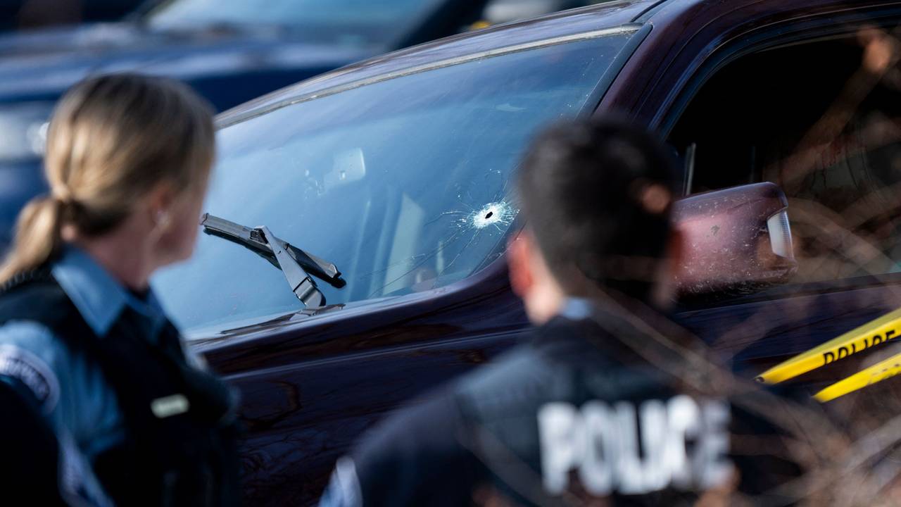 Polizeibeamte stehen vor einem Auto mit Einschussloch in der Windschutzscheibe