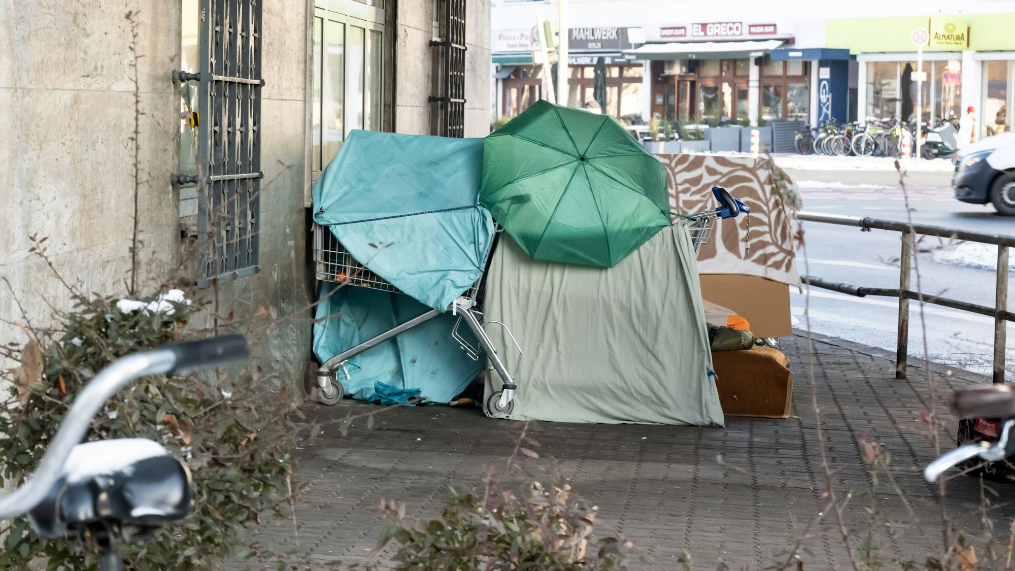Obdachlosen-Unterkunft im Winter mit Regenschirm und Einkaufswagen