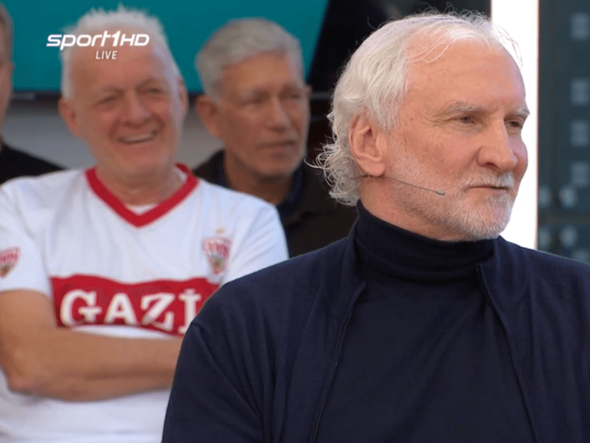 Rudi Völler sitzt mit Rollkragen-Pullover im „Doppelpass“.
